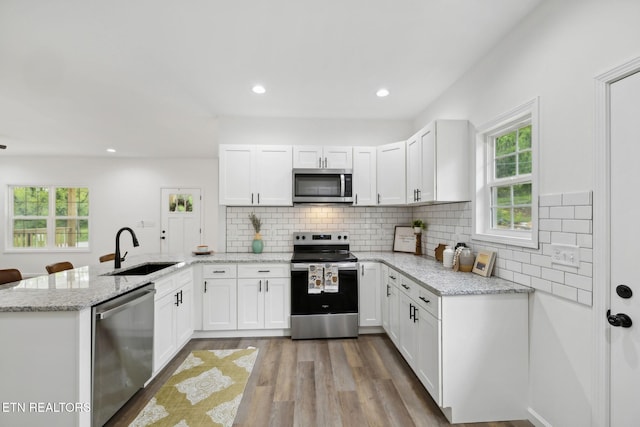 kitchen featuring a sink, a peninsula, white cabinetry, light wood finished floors, and stainless steel appliances