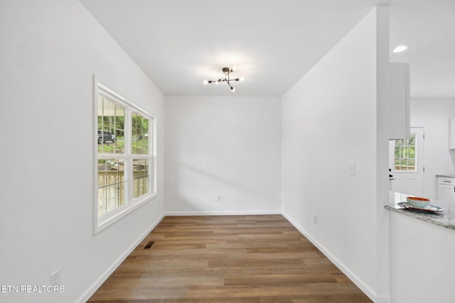 unfurnished dining area with wood finished floors, baseboards, visible vents, and a wealth of natural light