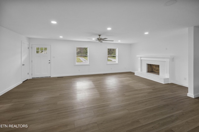 unfurnished living room with dark wood-style floors, recessed lighting, a brick fireplace, and baseboards