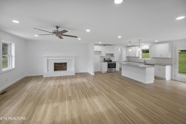 unfurnished living room featuring recessed lighting, a brick fireplace, a sink, and light wood finished floors