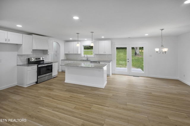 kitchen featuring light wood finished floors, white cabinets, custom range hood, stainless steel range with electric stovetop, and a sink