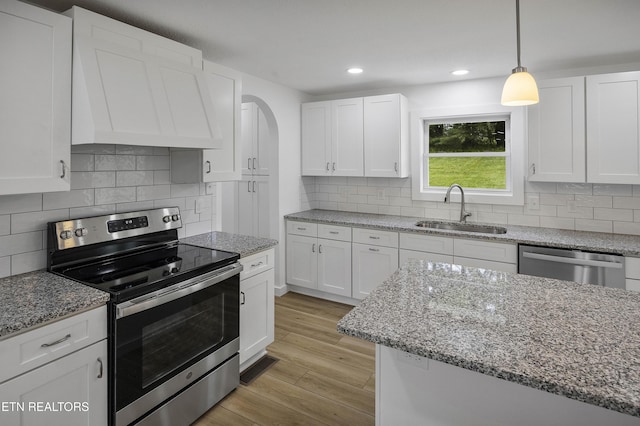 kitchen featuring stainless steel appliances, a sink, white cabinetry, light wood-type flooring, and custom range hood