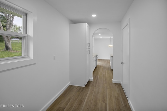 corridor featuring baseboards, arched walkways, wood finished floors, and recessed lighting