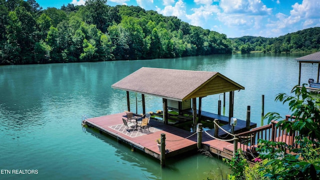 dock area with a water view, boat lift, and a view of trees