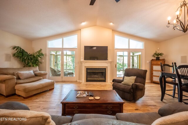 living area with lofted ceiling, a glass covered fireplace, plenty of natural light, and light wood-style flooring