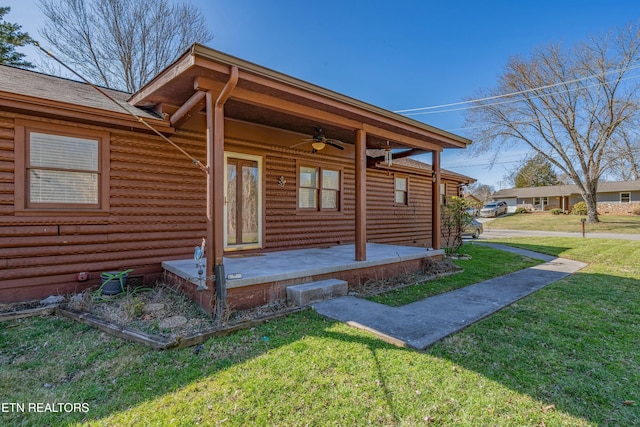 doorway to property featuring a ceiling fan, a patio area, a yard, and roof with shingles