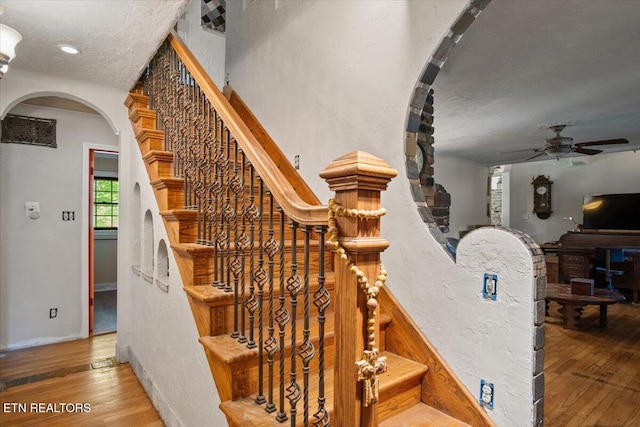 staircase with arched walkways, ceiling fan, a textured ceiling, a textured wall, and hardwood / wood-style flooring