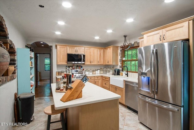 kitchen with a kitchen breakfast bar, stainless steel appliances, light countertops, light brown cabinets, and a sink