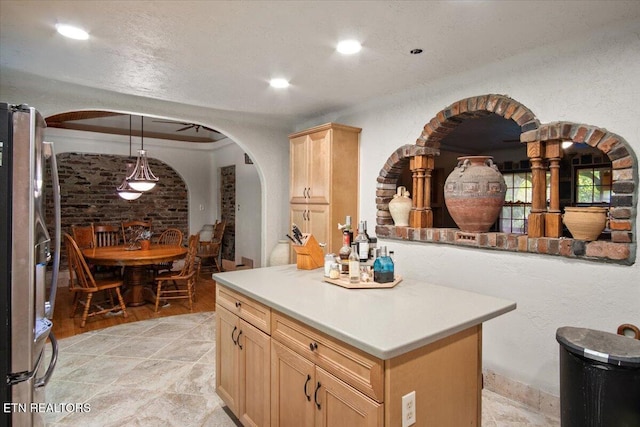 kitchen featuring arched walkways, decorative light fixtures, light countertops, light brown cabinetry, and freestanding refrigerator