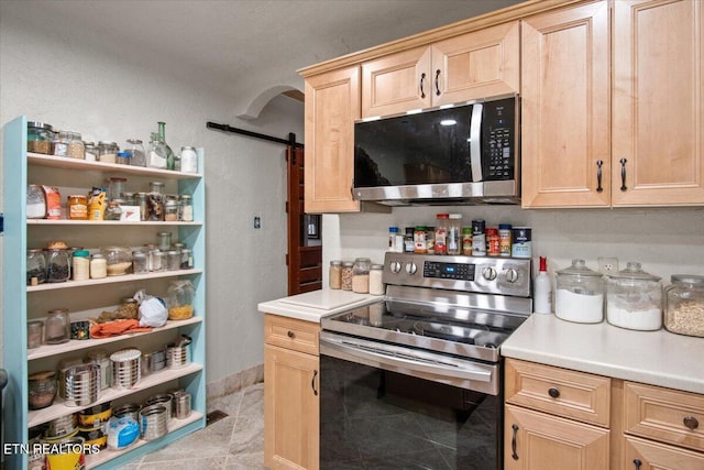 kitchen with appliances with stainless steel finishes, light brown cabinetry, light countertops, and a barn door