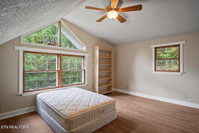 bedroom featuring lofted ceiling, multiple windows, a textured ceiling, and wood finished floors