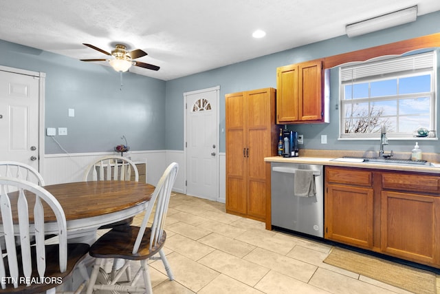 kitchen with a wainscoted wall, a sink, light countertops, brown cabinets, and dishwasher