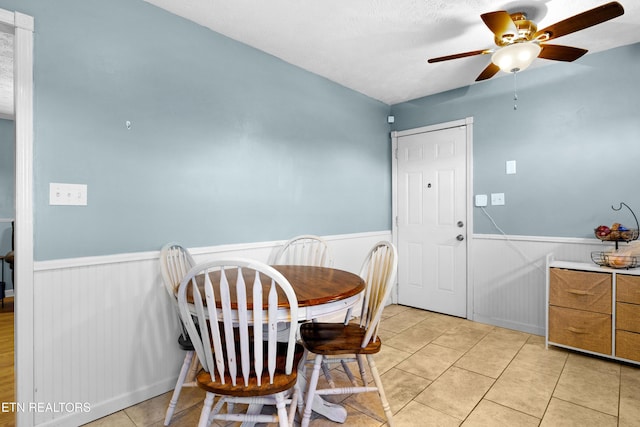 dining room with a wainscoted wall, light tile patterned floors, and a ceiling fan