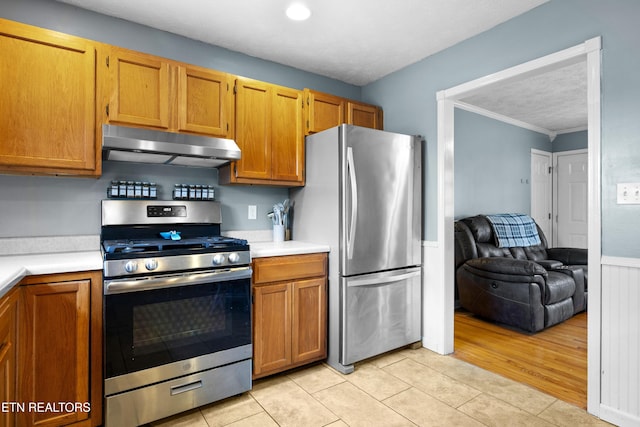 kitchen featuring light tile patterned floors, under cabinet range hood, light countertops, appliances with stainless steel finishes, and brown cabinets