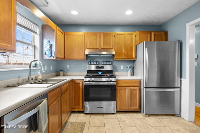 kitchen with light tile patterned floors, stainless steel appliances, light countertops, under cabinet range hood, and a sink