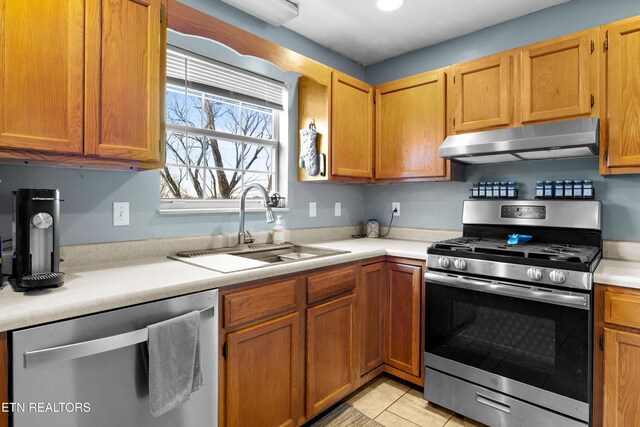 kitchen with light tile patterned floors, under cabinet range hood, a sink, light countertops, and appliances with stainless steel finishes