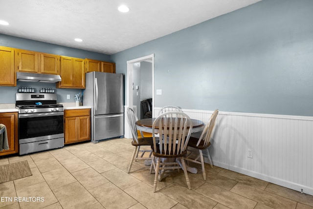 kitchen featuring light countertops, appliances with stainless steel finishes, wainscoting, and under cabinet range hood