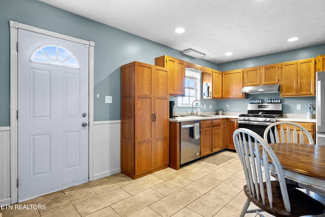 kitchen with under cabinet range hood, a wainscoted wall, a sink, light countertops, and appliances with stainless steel finishes