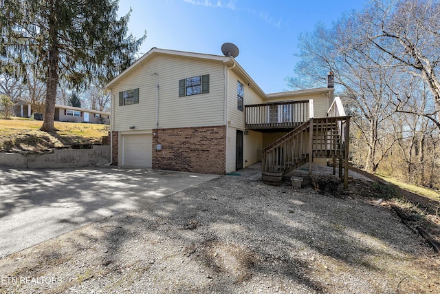 view of side of home featuring a deck, an attached garage, brick siding, driveway, and stairway