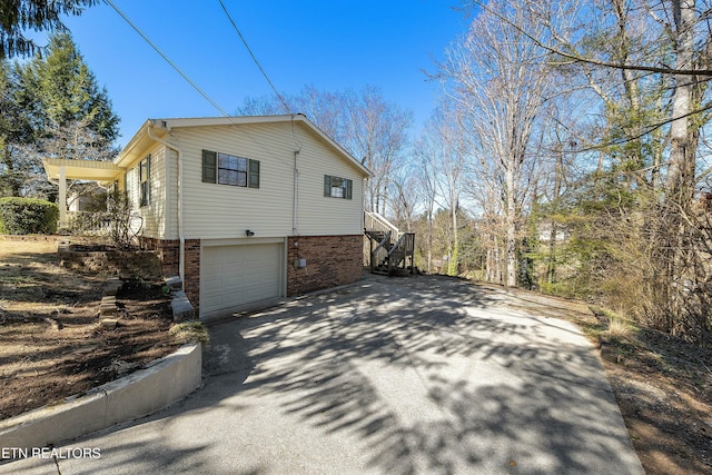 view of home's exterior with stairs, driveway, brick siding, and an attached garage