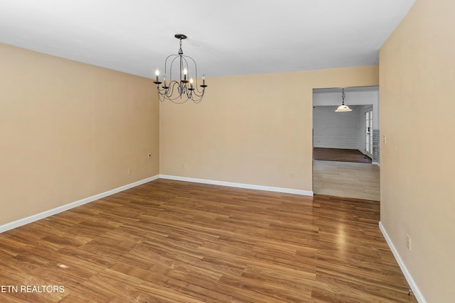 unfurnished room featuring baseboards, an inviting chandelier, and wood finished floors