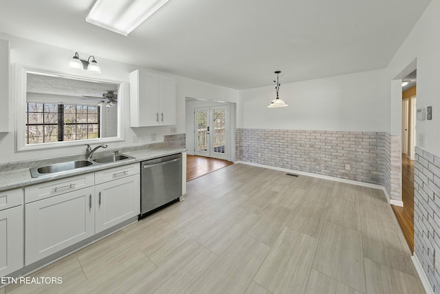 kitchen featuring white cabinets, wainscoting, a sink, light countertops, and stainless steel dishwasher