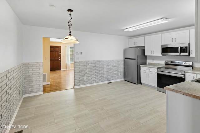 kitchen featuring light countertops, appliances with stainless steel finishes, wainscoting, white cabinetry, and brick wall