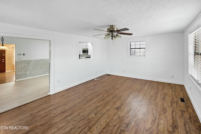 empty room with dark wood finished floors, visible vents, a ceiling fan, a textured ceiling, and baseboards