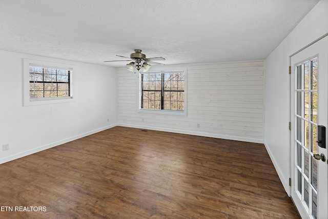 unfurnished room with wooden walls, a textured ceiling, and wood finished floors