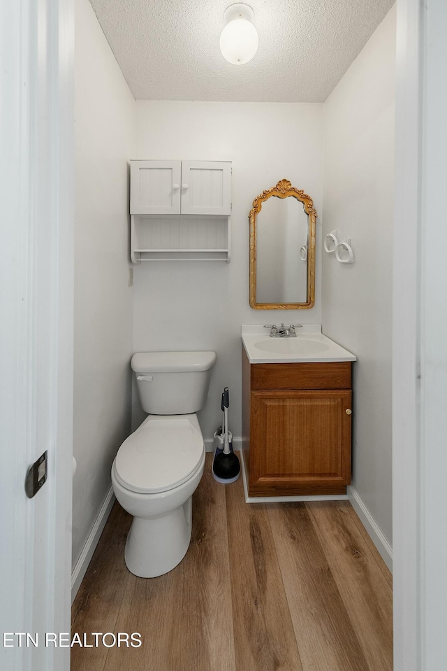 bathroom with baseboards, toilet, wood finished floors, a textured ceiling, and vanity