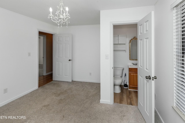 unfurnished bedroom with carpet, ensuite bath, baseboards, and an inviting chandelier