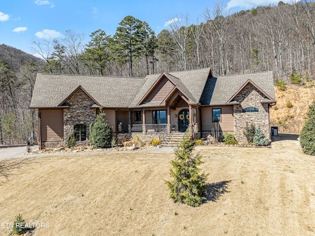 view of front facade with stone siding, a shingled roof, a front lawn, and covered porch