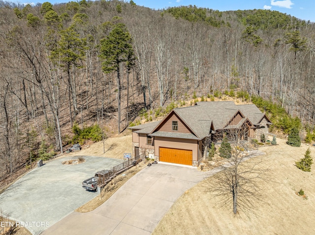 view of front facade featuring stone siding, concrete driveway, a forest view, and a garage