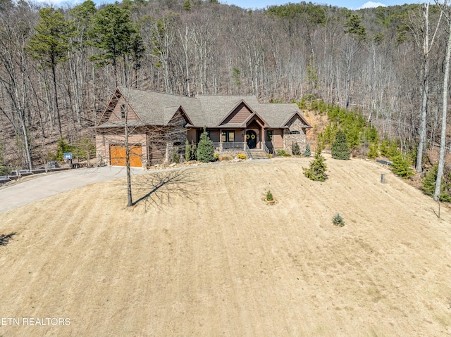 view of front of property featuring a garage, driveway, stone siding, and a view of trees