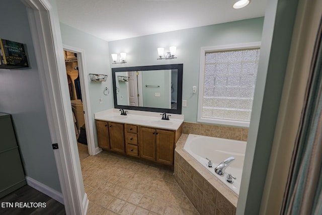 bathroom featuring double vanity, a sink, a spacious closet, and a bath