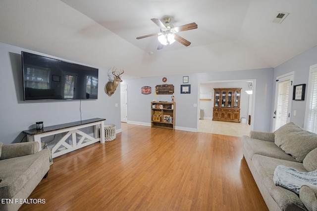 living area featuring visible vents, vaulted ceiling, ceiling fan, light wood-type flooring, and baseboards