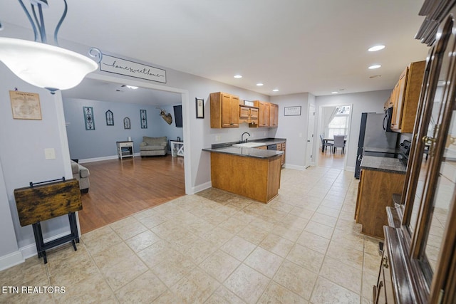 kitchen with dark countertops, brown cabinetry, open floor plan, and a sink