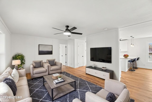 living area featuring ceiling fan, light wood-style flooring, and baseboards