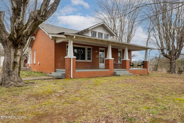 view of front of house with a porch, brick siding, and a front yard