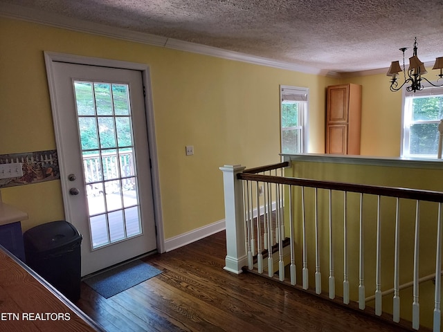 doorway with a textured ceiling, baseboards, ornamental molding, dark wood finished floors, and an inviting chandelier