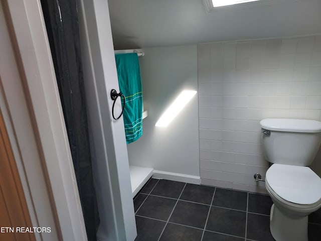 bathroom with a shower, tile patterned flooring, toilet, and tile walls