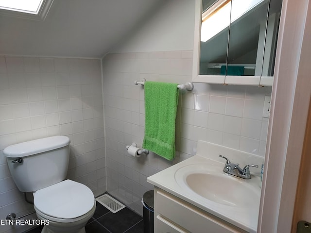 bathroom featuring toilet, visible vents, vanity, vaulted ceiling, and tile walls