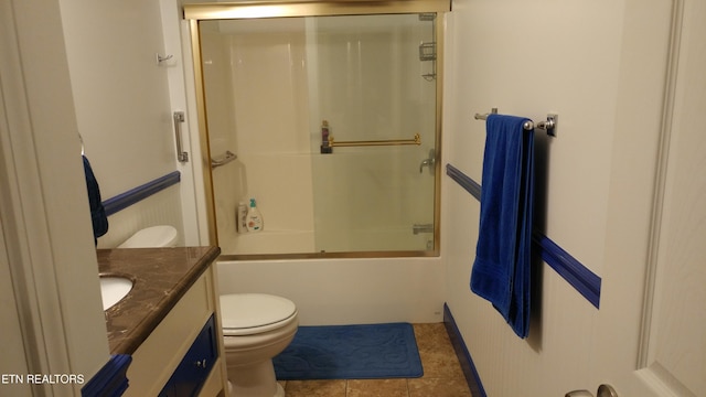 bathroom with bath / shower combo with glass door, wainscoting, toilet, tile patterned flooring, and vanity