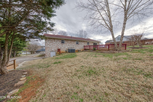 back of house featuring brick siding, a yard, a wooden deck, and central air condition unit