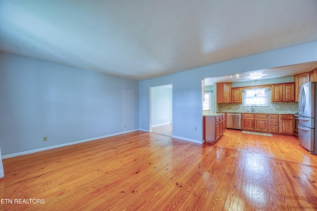 kitchen featuring brown cabinets, backsplash, light wood-style flooring, appliances with stainless steel finishes, and a sink