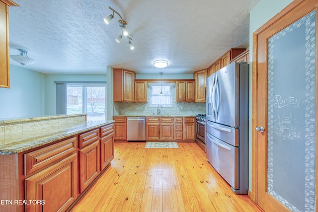 kitchen with brown cabinets, decorative backsplash, appliances with stainless steel finishes, light wood-style floors, and a sink