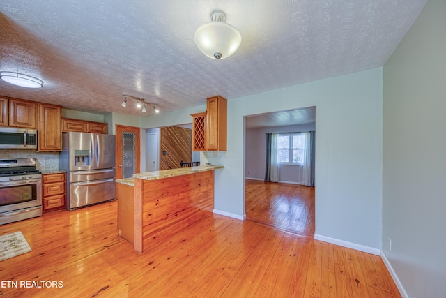 kitchen with light wood-style flooring, stainless steel appliances, a peninsula, baseboards, and brown cabinetry