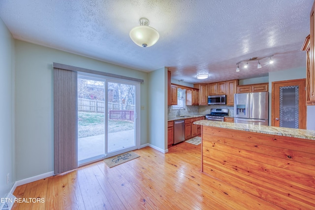 kitchen with a sink, light wood-style floors, light countertops, appliances with stainless steel finishes, and brown cabinets