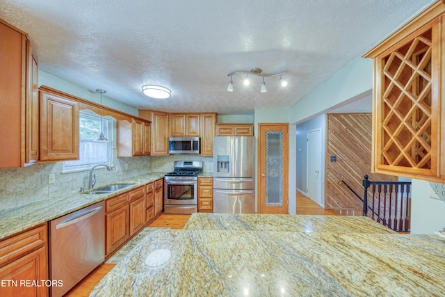 kitchen with stainless steel appliances, a sink, backsplash, light stone countertops, and light wood finished floors