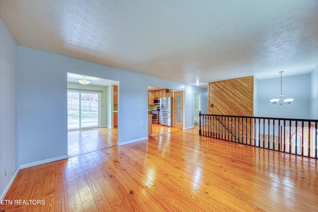 unfurnished room with light wood finished floors, a textured ceiling, baseboards, and a notable chandelier